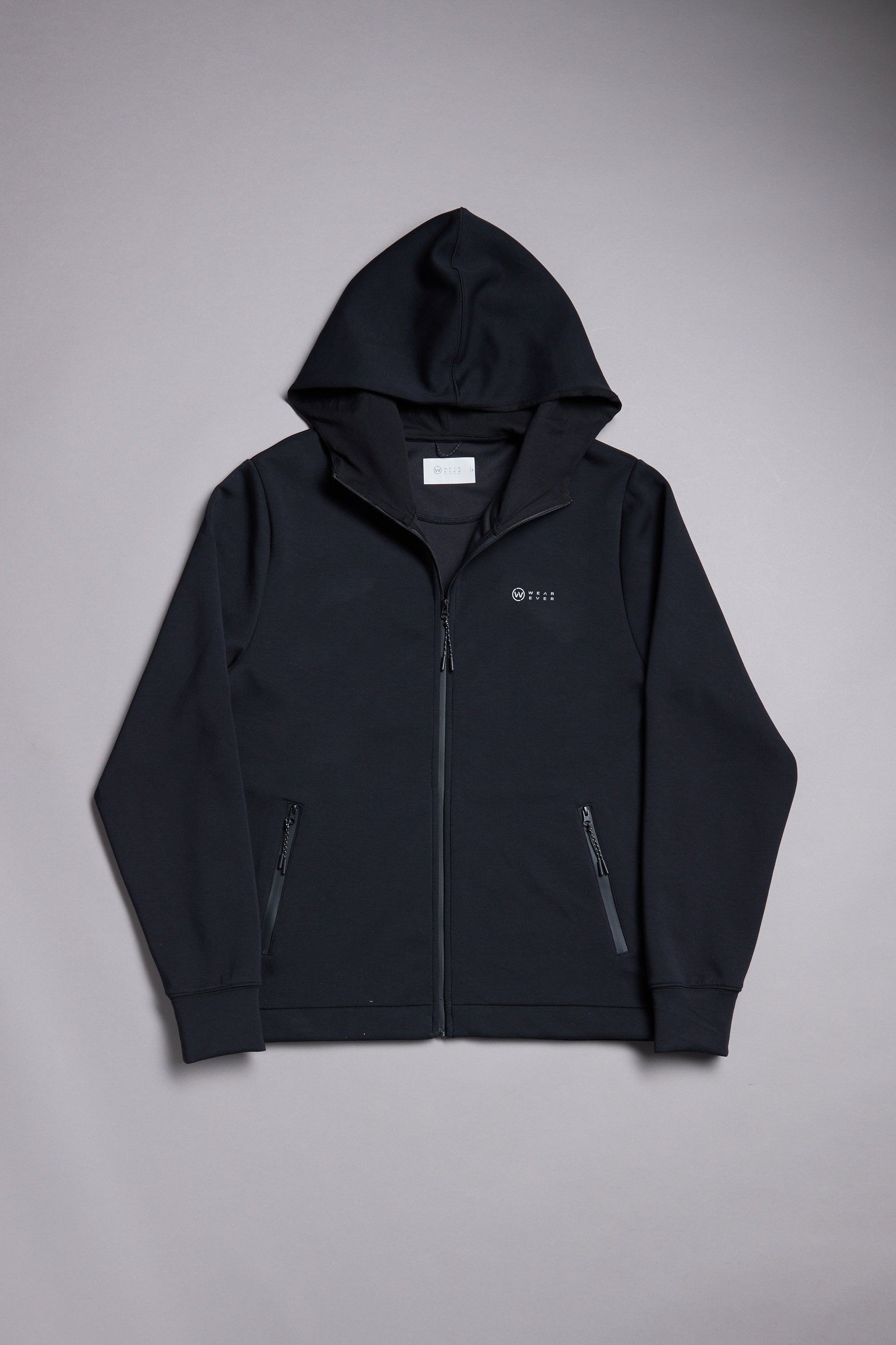 The WearEver Altitude Hoody by WearEver is a black tech fleece zip-up jacket with long sleeves, two front zip pockets, and a small logo/text on the left chest—an ideal everyday layer, shown laid flat on a light gray background.