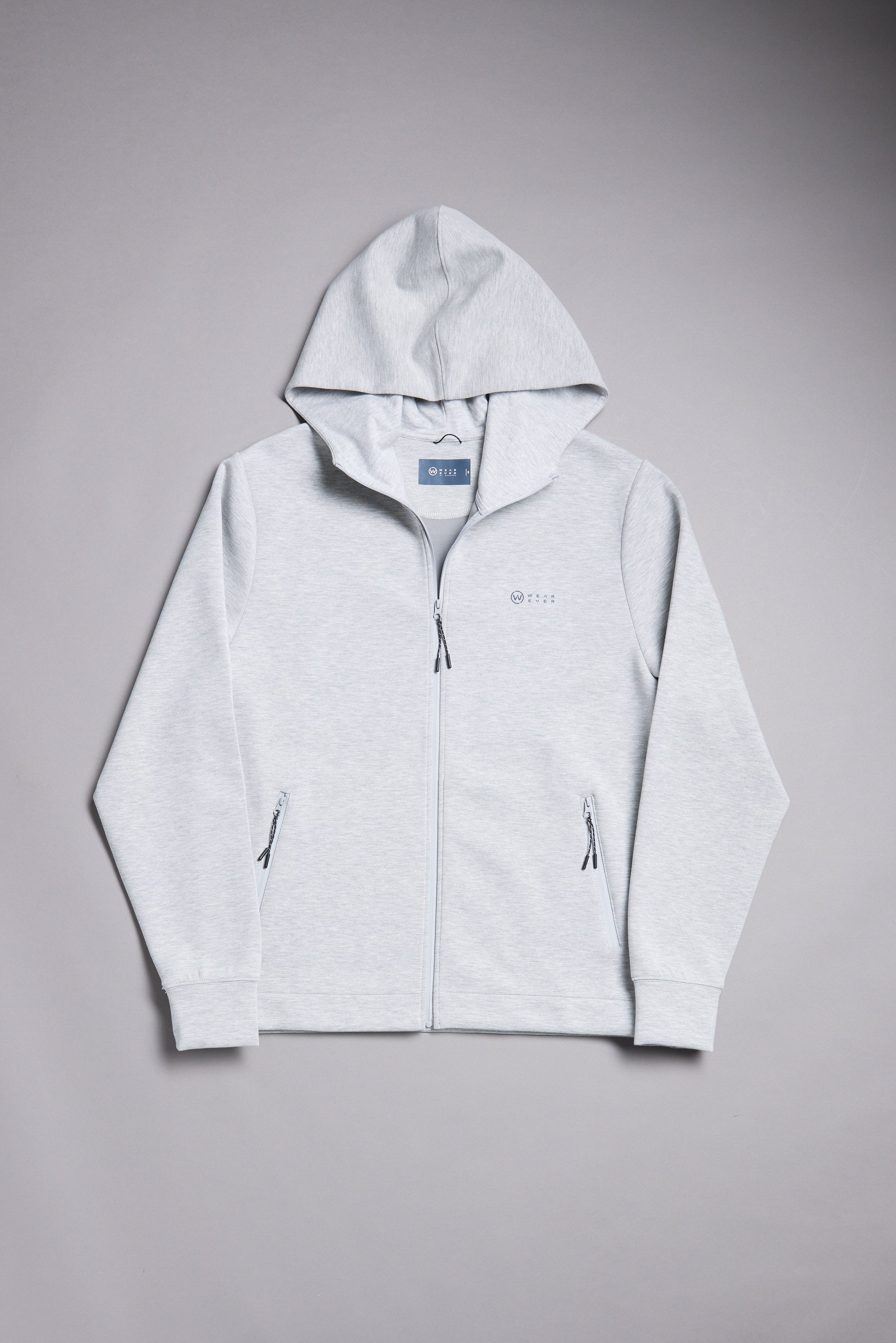 The WearEver Altitude Hoody by WearEver is a light gray, full-zip lightweight hoodie featuring a hood, front pockets, and subtle branding on the left chest, shown laid flat on a plain gray background.