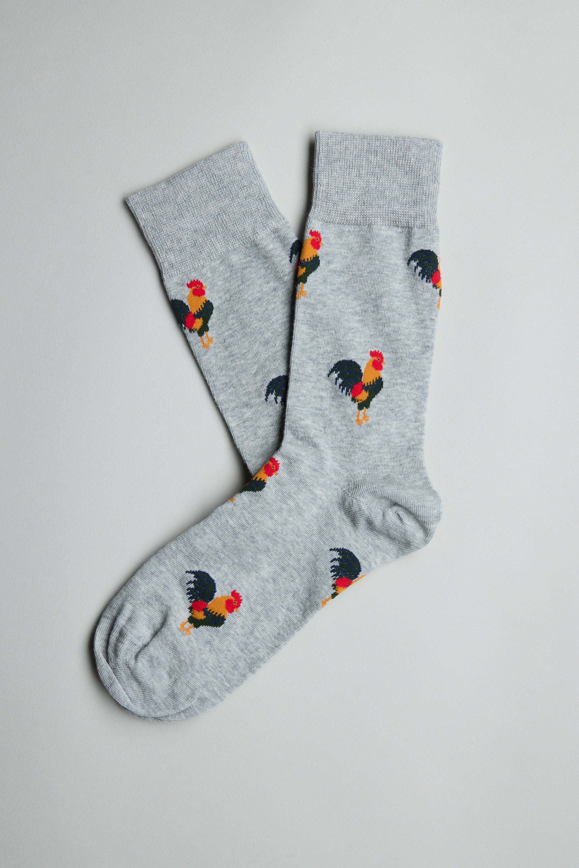 The Barkers Willis Rooster Sock is a playful light gray cotton blend sock featuring a colorful repeating rooster pattern with red, yellow, and black details, displayed flat on a plain white background.