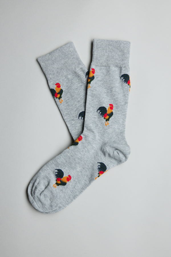 The Barkers Willis Rooster Sock is a playful light gray cotton blend sock featuring a colorful repeating rooster pattern with red, yellow, and black details, displayed flat on a plain white background.