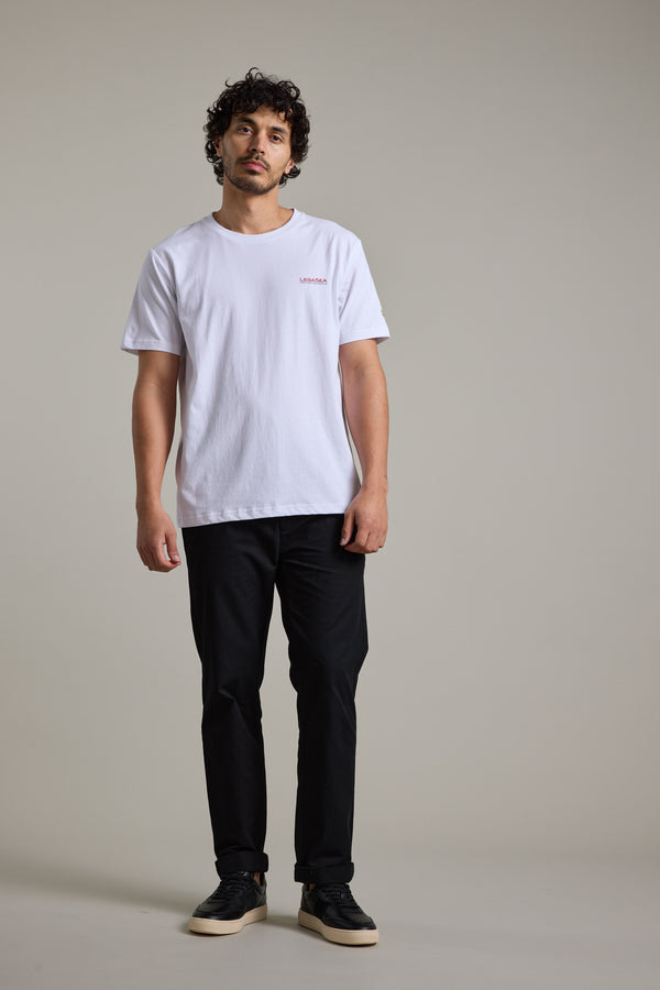Man in Legasea Brand Tee and black pants stands against a plain gray background.