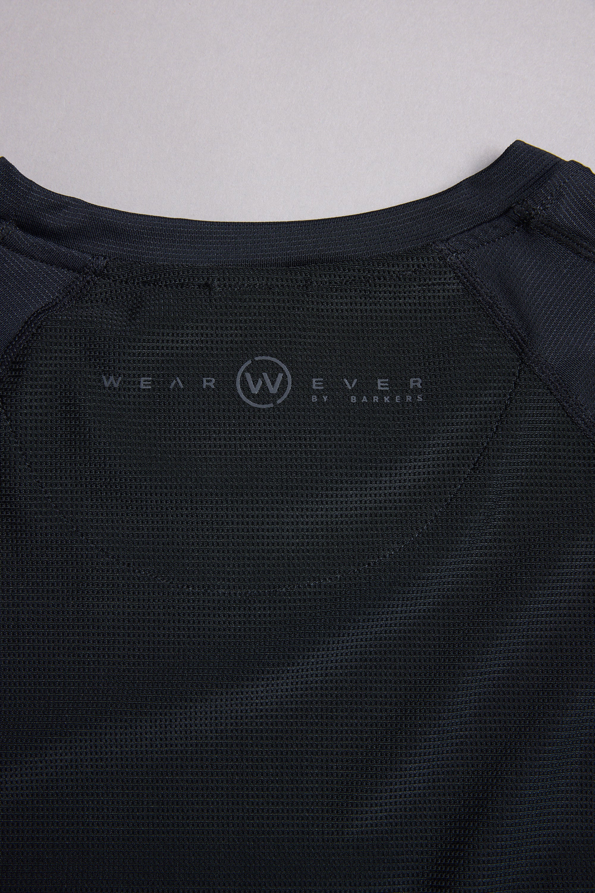Close-up of the inside back collar of a black WearEver Pulse Tee by WearEver, featuring a circular W logo and brand text printed on quick-dry performance mesh fabric.