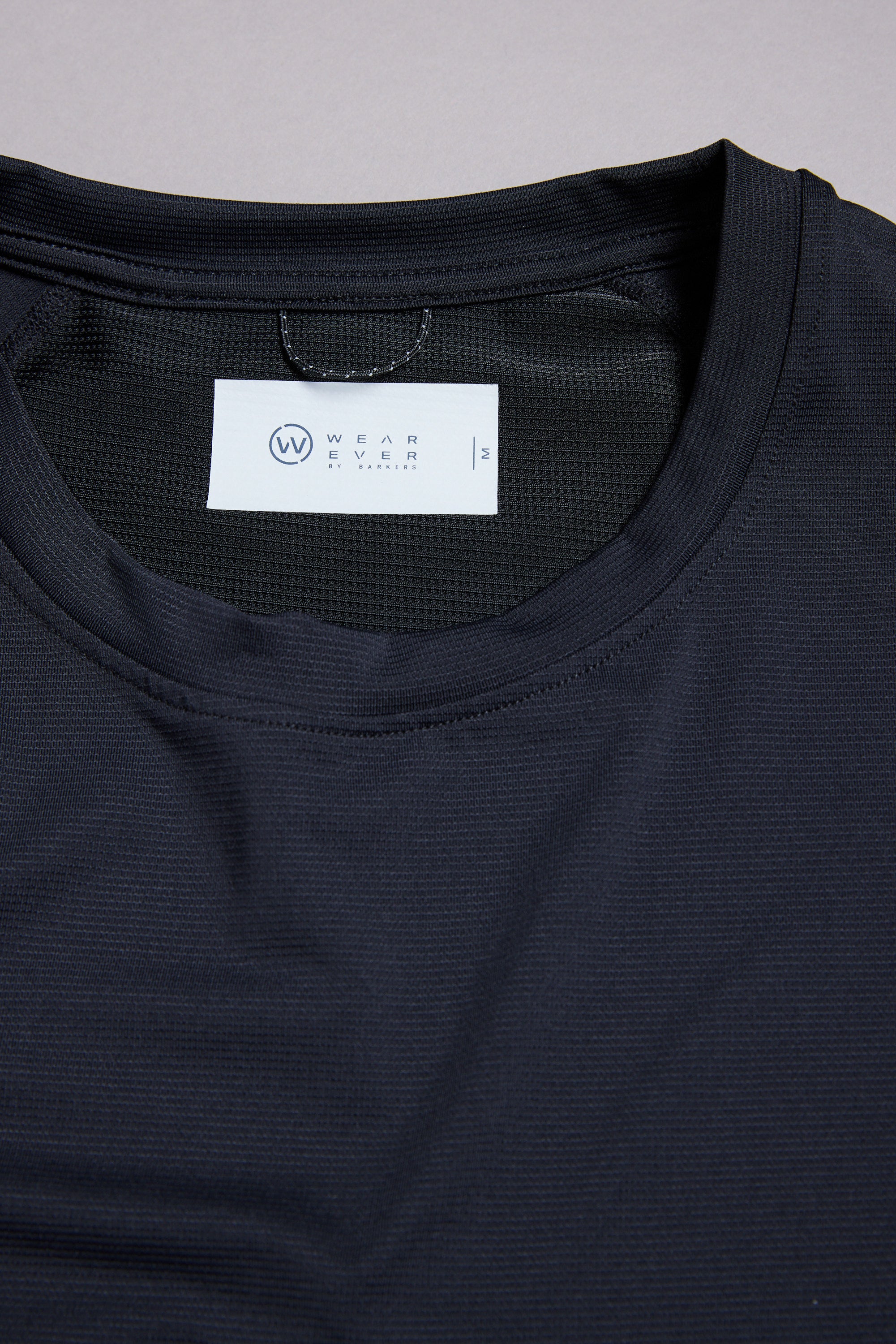 A close-up of the black WearEver Pulse Tee, an athletic t-shirt with a crew neck, crafted from quick-dry fabric and featuring a white label inside the collar showing the WearEver brand and size medium.