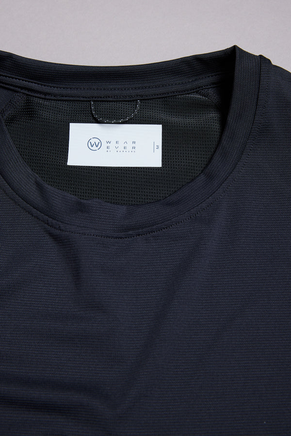 A close-up of the black WearEver Pulse Tee, an athletic t-shirt with a crew neck, crafted from quick-dry fabric and featuring a white label inside the collar showing the WearEver brand and size medium.