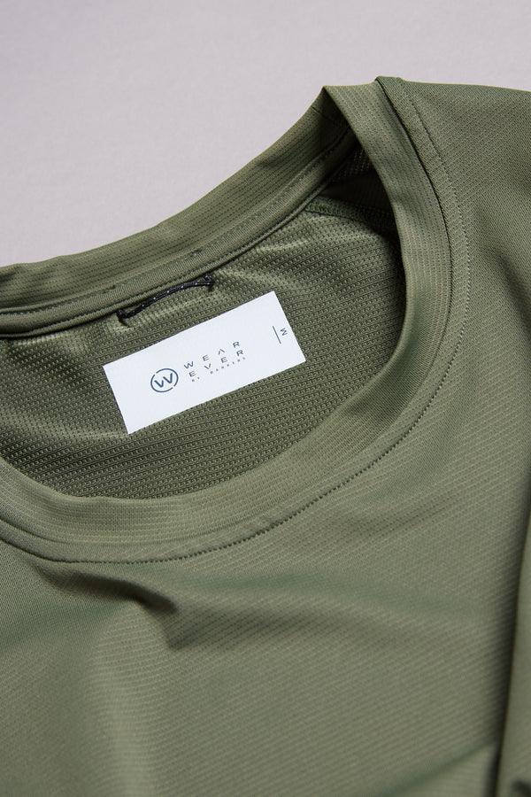 Close-up of the WearEver Pulse Tee, an olive green performance t-shirt featuring a white inner collar label with brand and size L. The fabric displays a subtle textured pattern and offers moisture-wicking properties.