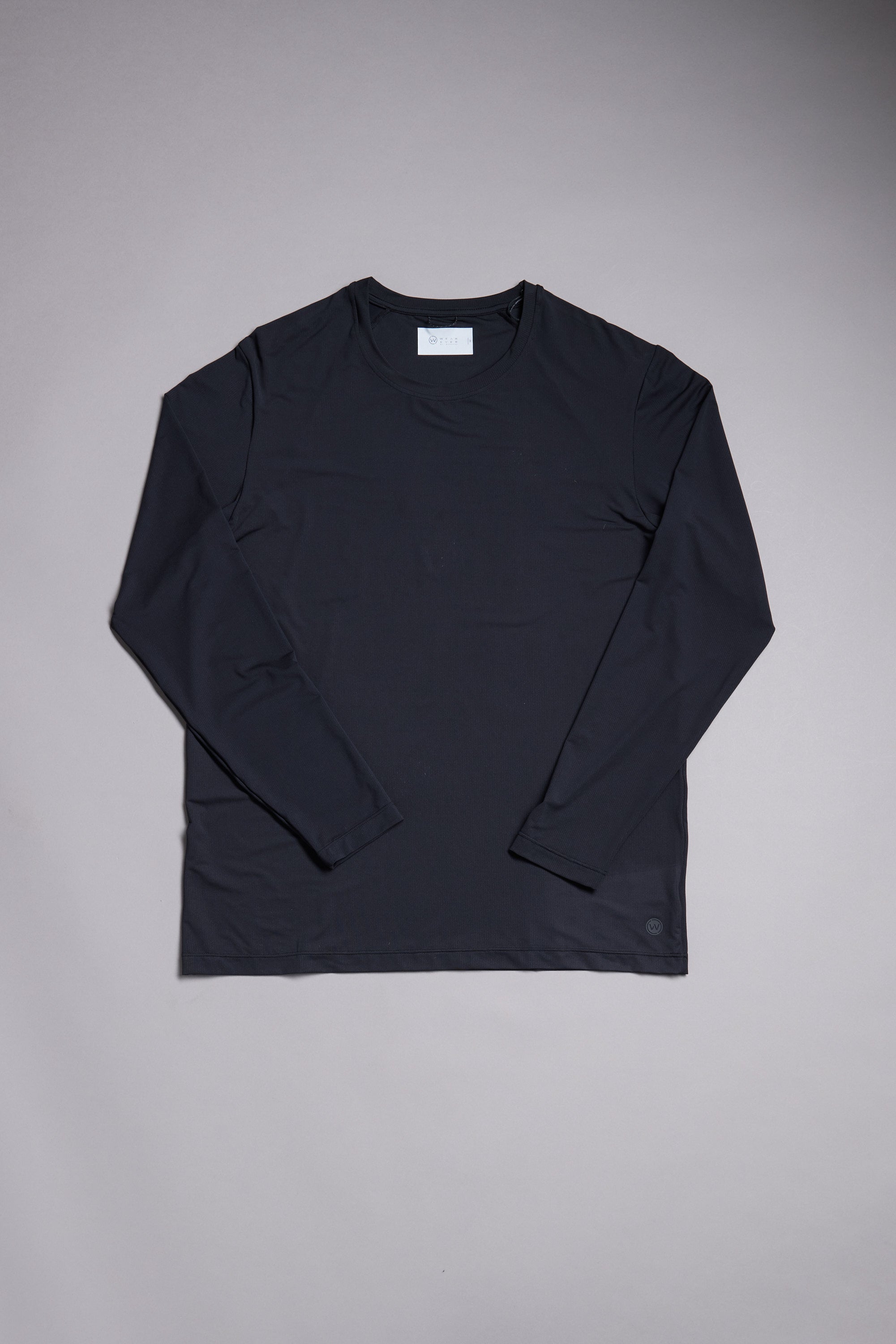 The WearEver Pulse Long Sleeve Tee by WearEver, in black, features moisture-wicking fabric. It’s displayed flat on a light gray background with neatly arranged sleeves and a white tag visible at the collar.