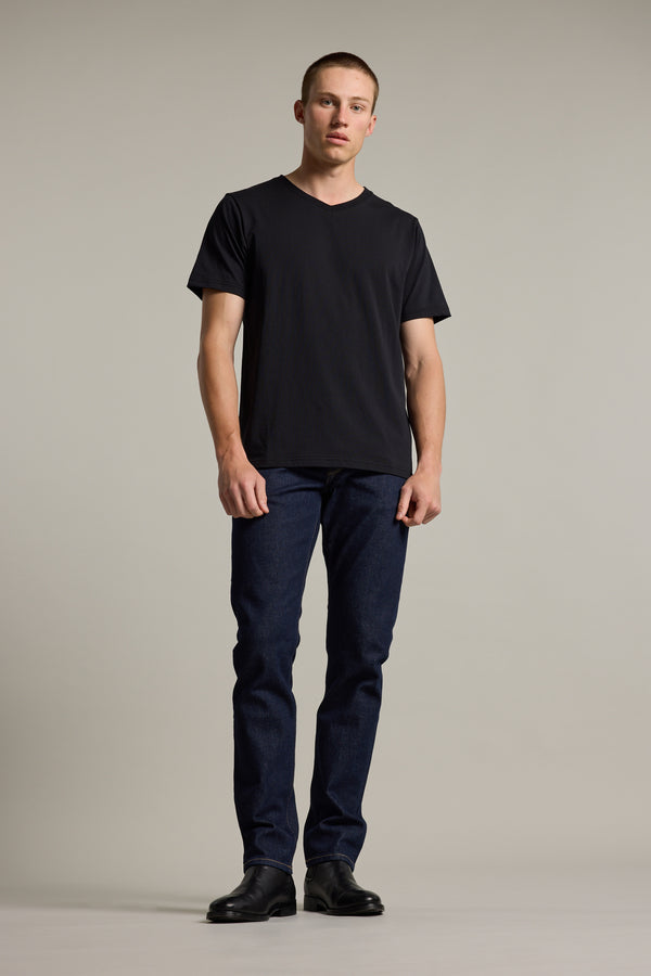 A man stands against a plain light background, wearing the Barkers Organic Cotton V Neck Tee, dark blue jeans, and black shoes. He looks at the camera with a neutral expression, showcasing an everyday essential style.