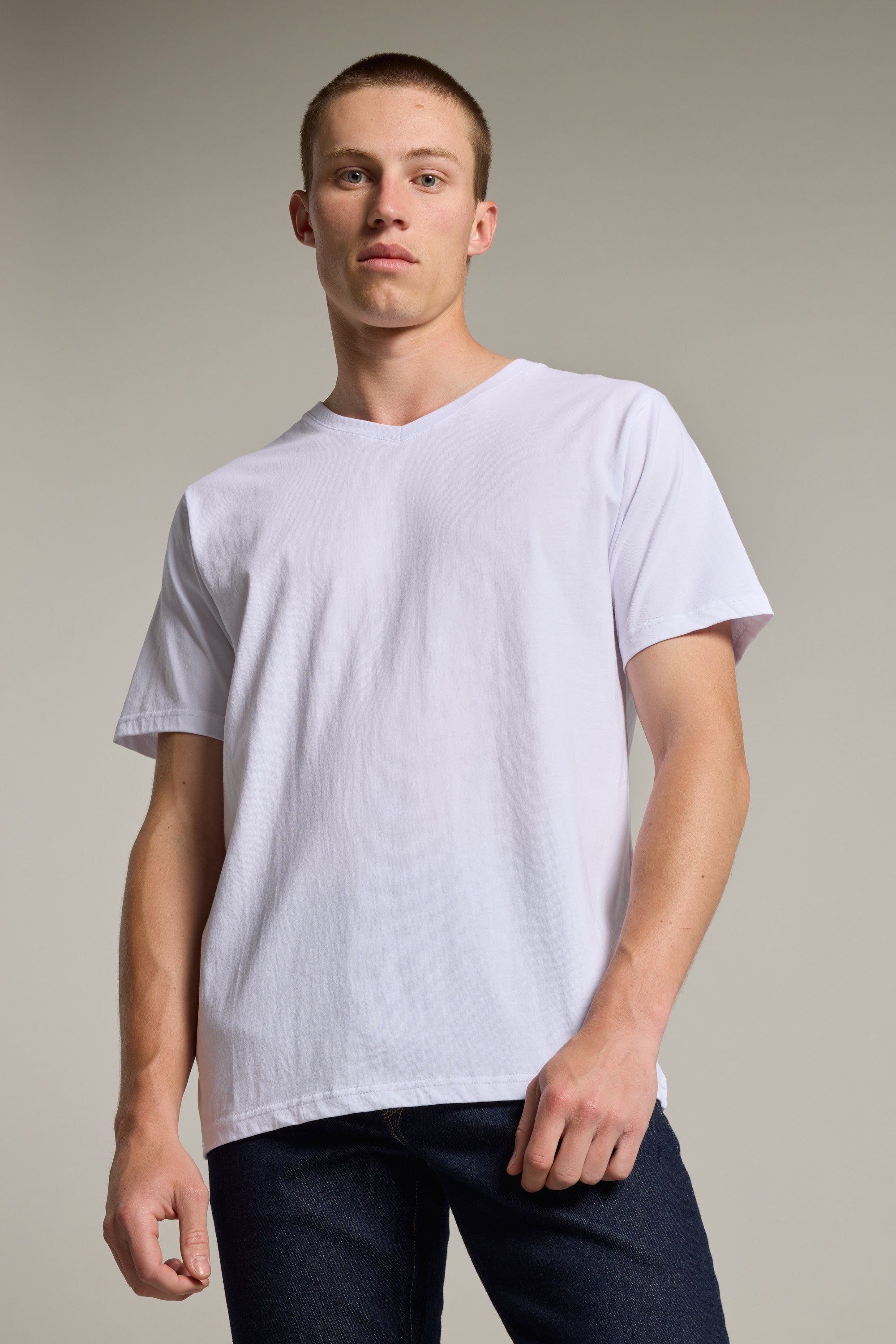 A young man with short hair stands confidently against a plain background, wearing the Barkers Organic Cotton V Neck Tee—an everyday essential—paired with dark jeans.
