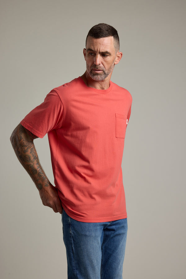 A man with short hair and right arm tattoos wears a Barkers Summer Soul Sessions Print Tee and blue jeans. He stands facing left, looking off to the side, against a neutral background.
