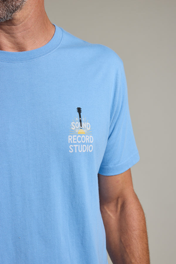 A person wearing a light blue Barkers BMC Sound Sessions Print Tee, featuring a Sound Record Studio guitar logo on the left chest. Only the lower half of the face, neck, and upper torso are visible.