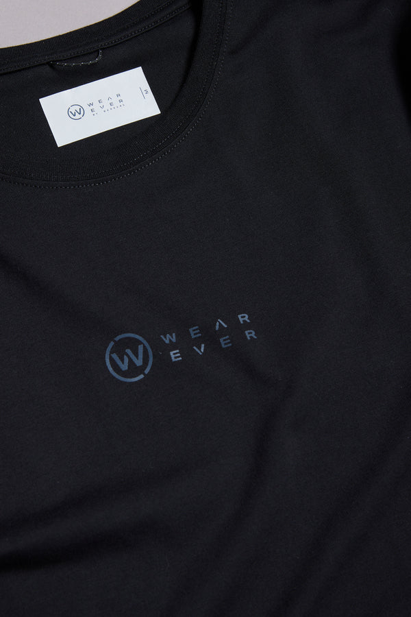 A close-up of the WearEver Outbound T-Shirt, a black cotton stretch tee featuring the dark blue WearEver logo on the chest and a white branded label inside the neckline.