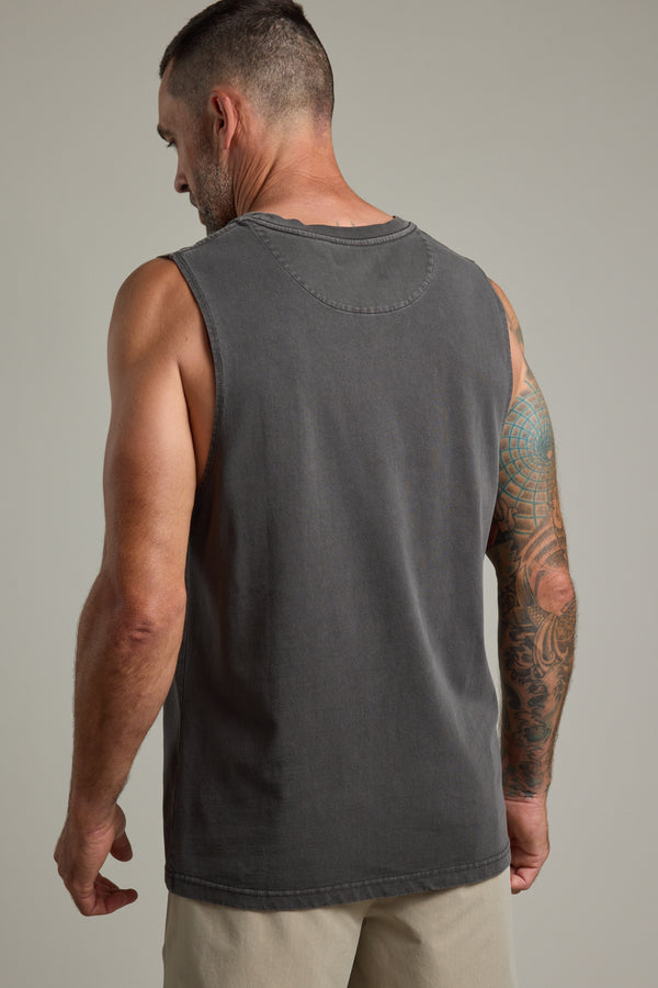A man with short dark hair and a tattooed right arm wears the Barkers Newton Washed Singlet and light shorts, standing with his back to the camera against a plain background.