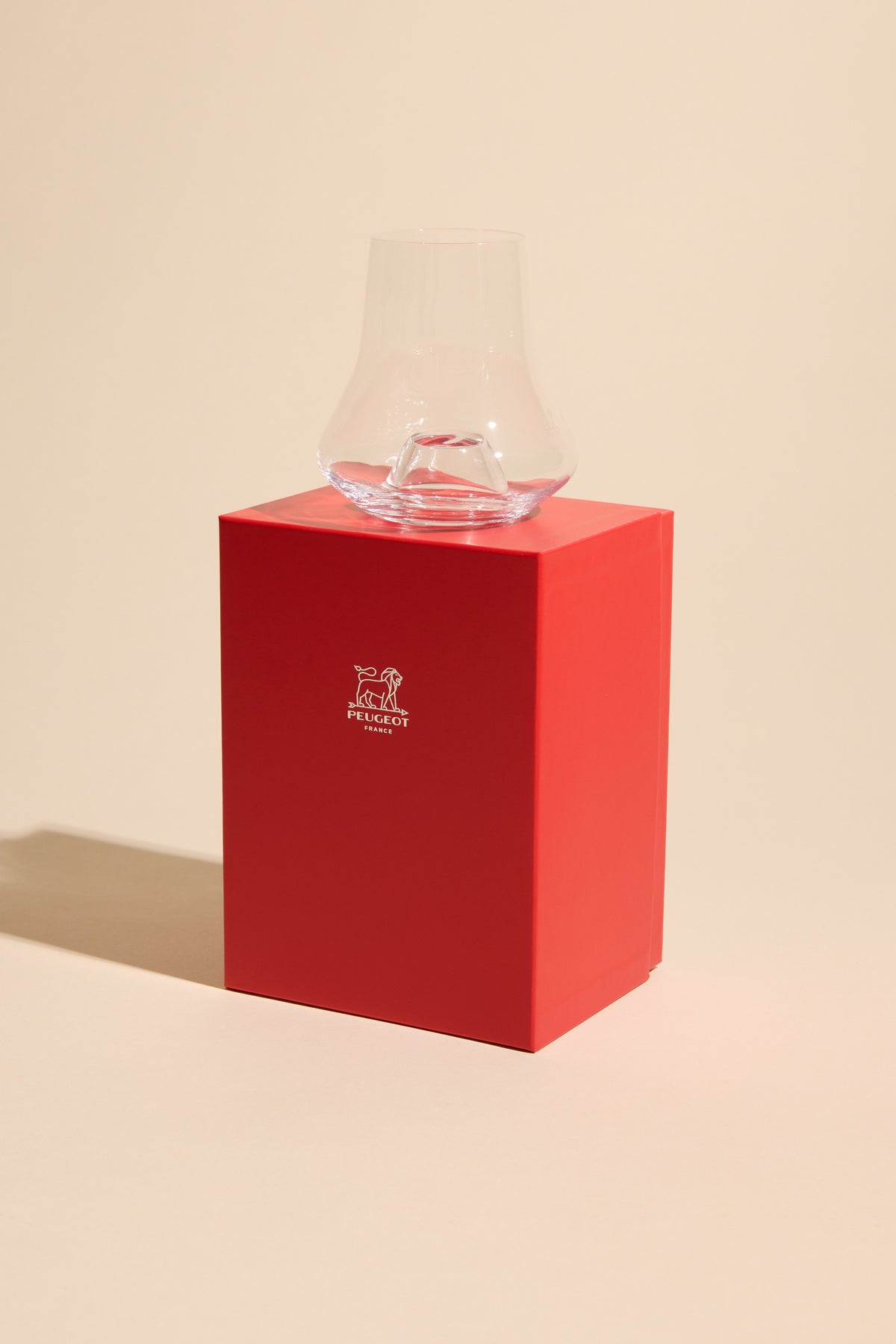 A Whisky Glass Individual by Other sits atop a tall red box, set against a beige background.