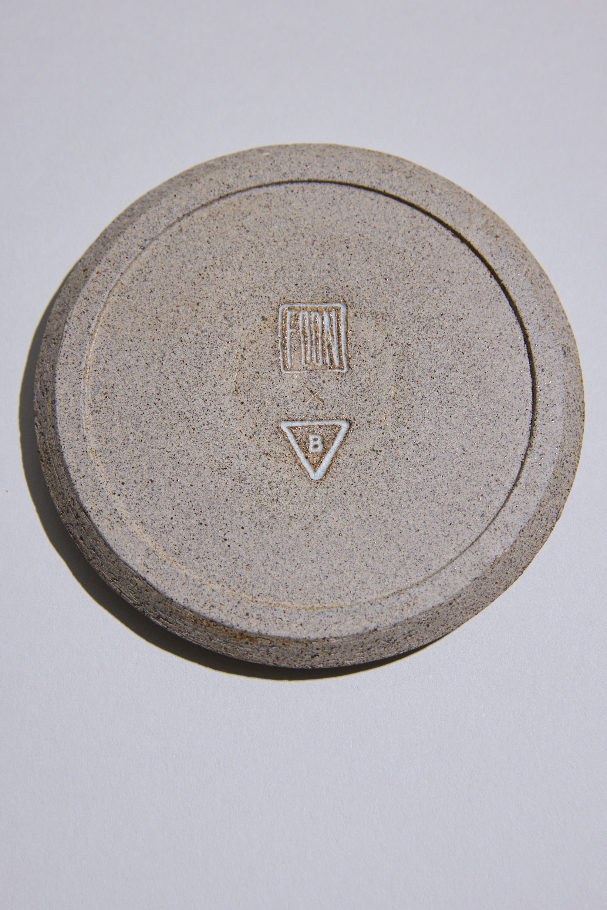 The Studio Foon Incense Dish by Other is a round, speckled New Zealand ceramic piece with a raised rim and natural clay finish, featuring a FRONT rectangle and triangle B symbol, displayed on a plain white surface.