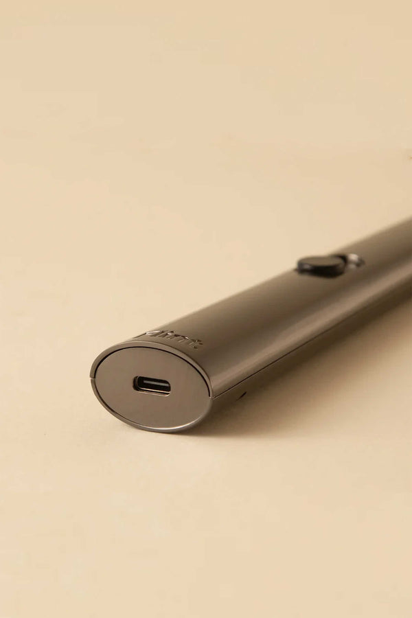A close-up of the Flint Rechargeable Lighter 2.0 by Flint, featuring a sleek metallic design, USB-C charging port, and a small side button, resting on a beige surface.