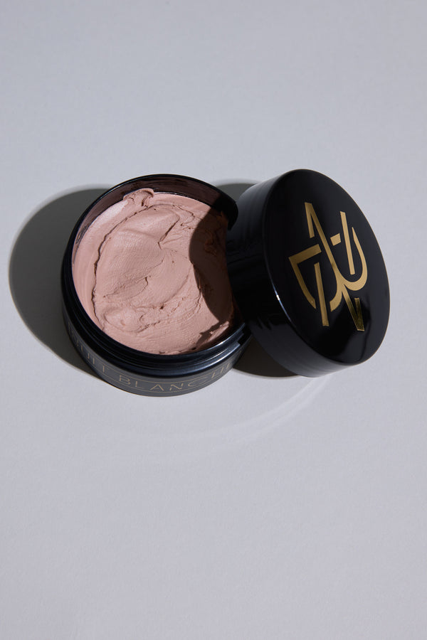 A black container with gold "Other" lettering on the lid sits on a light gray surface, revealing smooth, pinkish-beige Nuit Blanche Clay—a hair styling product made in New Zealand.