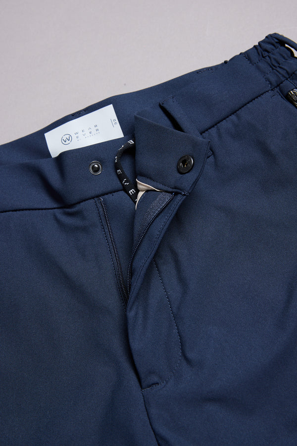 Close-up of WearEver Long Game Pant by WearEver: navy blue trousers with open waistband, displaying button, zipper, and label—highlighting chino-inspired style for comfortable, stylish travel.