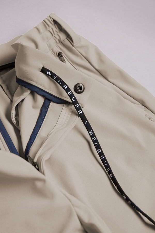 A close-up of the WearEver Long Game Pant showcases a beige quick-dry fabric with snap button and black drawstring featuring “WE’REVER.” Blue trim accents line the interior, reflecting technical details from WearEver’s lightweight performance pants.