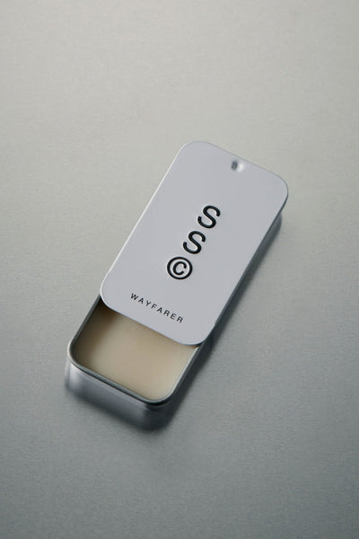 A rectangular metal tin with a sliding lid, partially open to reveal Solid State's Wayfarer solid cologne. The lid features minimalist branding and text on a light background, reflecting true Australian fragrance style.